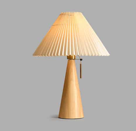 Une lampe de chevet avec un pied en bois en forme de cône, un abat-jour plissé beige sur fond gris.