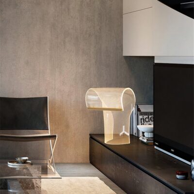 Un salon avec une chaise noir, une table en verre, un meuble blanc et noir sur la droite. Posé sur le meuble une lampe art déco transparente.