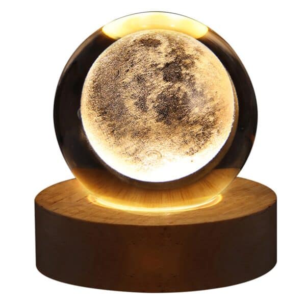 Une lampe en boule de cristal sur un socle en bois rond. Motif lune éclairé par le socle. Sur fond blanc.