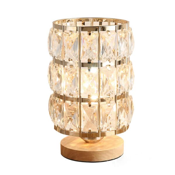 Une lampe de chevet en cristal de forme cylindrique sur un socle en bois rond. Sur fons blanc.