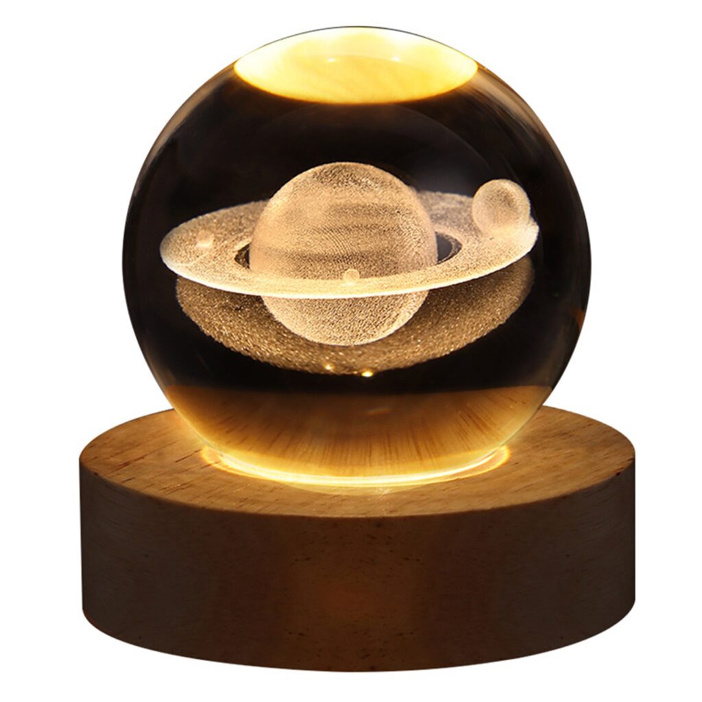Une lampe boule de cristal sur un socle en bois rond. Un motif saturne à l'intérieur de la boule éclairé par le socle. Sur fond blanc.