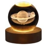 Une lampe boule de cristal sur un socle en bois rond. Un motif saturne à l'intérieur de la boule éclairé par le socle. Sur fond blanc.