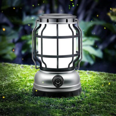 lampe de camping solaire LED style lanterne, posée sur de l'herbe dans la pénombre, elle est allumée