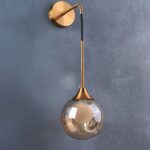 Lampe murale de couleur dorée, tombant vers le bas comme une goutte, installée sur un mur gris