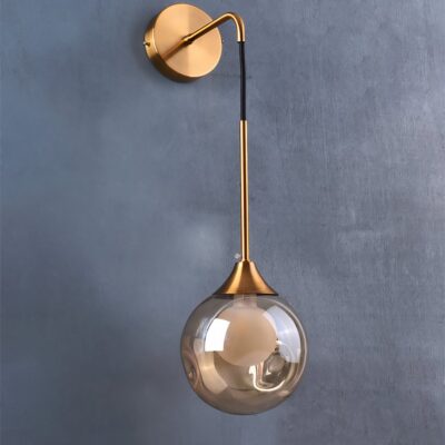 Lampe murale de couleur dorée, tombant vers le bas comme une goutte, installée sur un mur gris