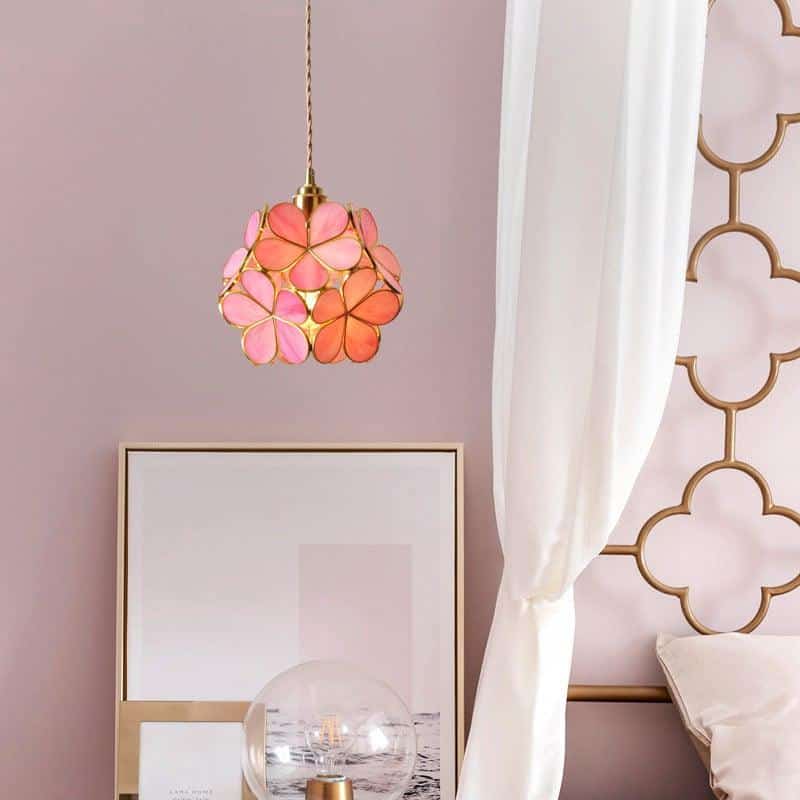 Dans une chambre près d'un lit, un luminaire suspendu en forme de fleur rose et dorée, se trouve devant un miroir