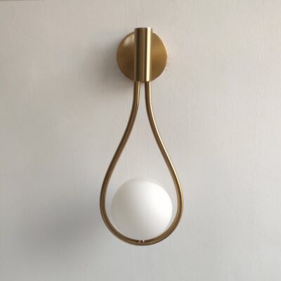 lampe murale degn en forme de goutte accrochée à un mur , elle est de couleur dorée avec une boule blanche qui semble suspendue