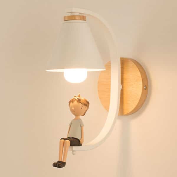 installée sur un mur, une lampe planche sous laquelle un crochet se prolonge et une poupée représentant un petit garçon se trouve assis au bout