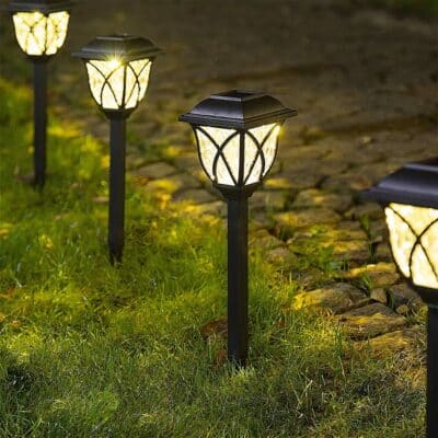 lot de lampes solaire allumé plantées dans un jardin sur de la pelouse verte. Derrière, il y a un chemin pavé.