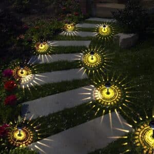 Une allée de nuit parsemée de lampe solaire plantée au sol, elles sont allumées et éclairent avec des motifs jaune design au sol.