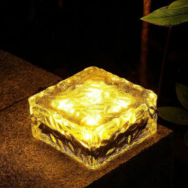 Une lampe en forme de cube transparent allumé posé sur un support marron.