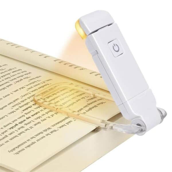 Lampe de lecture allumée accrochée à la page d'un livre, sur fond blanc.