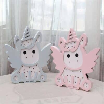 Lampe licorne bébé avec des ailes rose ou bleue présentée sur un tissu blanc