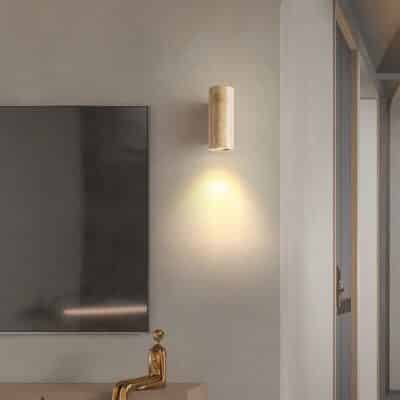 Lampe murale cylindrique en pierre présente sur un mur beige dans un salon