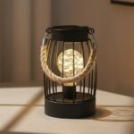 Cette lampe de table lanterne vintage nomade révèle sa cage filaire noire en fer avec son anse en corde de jute et son ampoule globe LED pour créer votre ambiance tamisée nomade et chaleureuse.