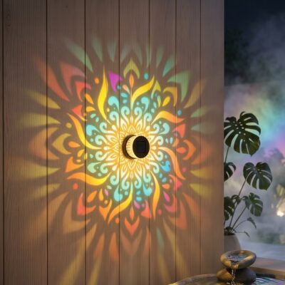 La lampe solaire mandala couleur chaude ou rgb projetant un motif floral multicolore sur cloture bois de jardin.