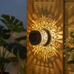 lampe solaire mandala papillon lumière chaude fixée sur poteau bois avec projection dorée.