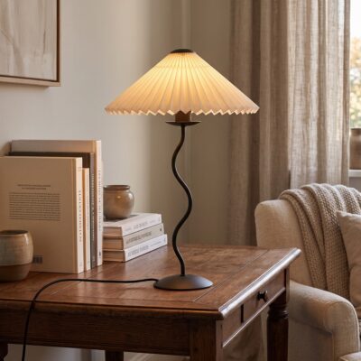 Une lampe ondulée en parapluie plissé au style danois posée sur une table en bois, avec un abat-jour beige et une lumière chaude dans une chambre calme.