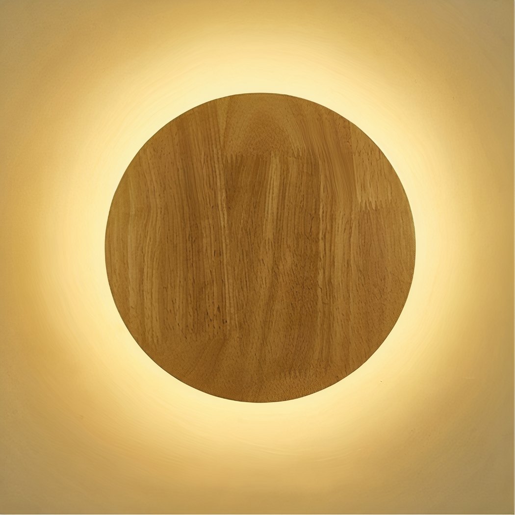 Une applique murale ronde en bois avec éclairage indirect LED diffuse une lumière chaude autour d’un disque en bois sur un mur beige.