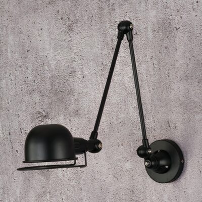 Une applique murale industrielle articulée style atelier vintage noire, fixée sur un mur gris, avec un bras réglable et un abat-jour orientable.