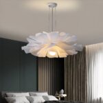 Une suspension fleur design en pétales contemporains blanche, en forme de grande fleur lumineuse suspendue au plafond, dans une chambre moderne avec lit gris et rideaux élégants.