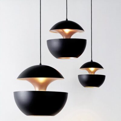 Trois suspensions de plafond, dont un lustre boule design noir et doré style contemporain, en forme de demi-sphères noires avec intérieur doré, éclairant doucement un fond blanc.
